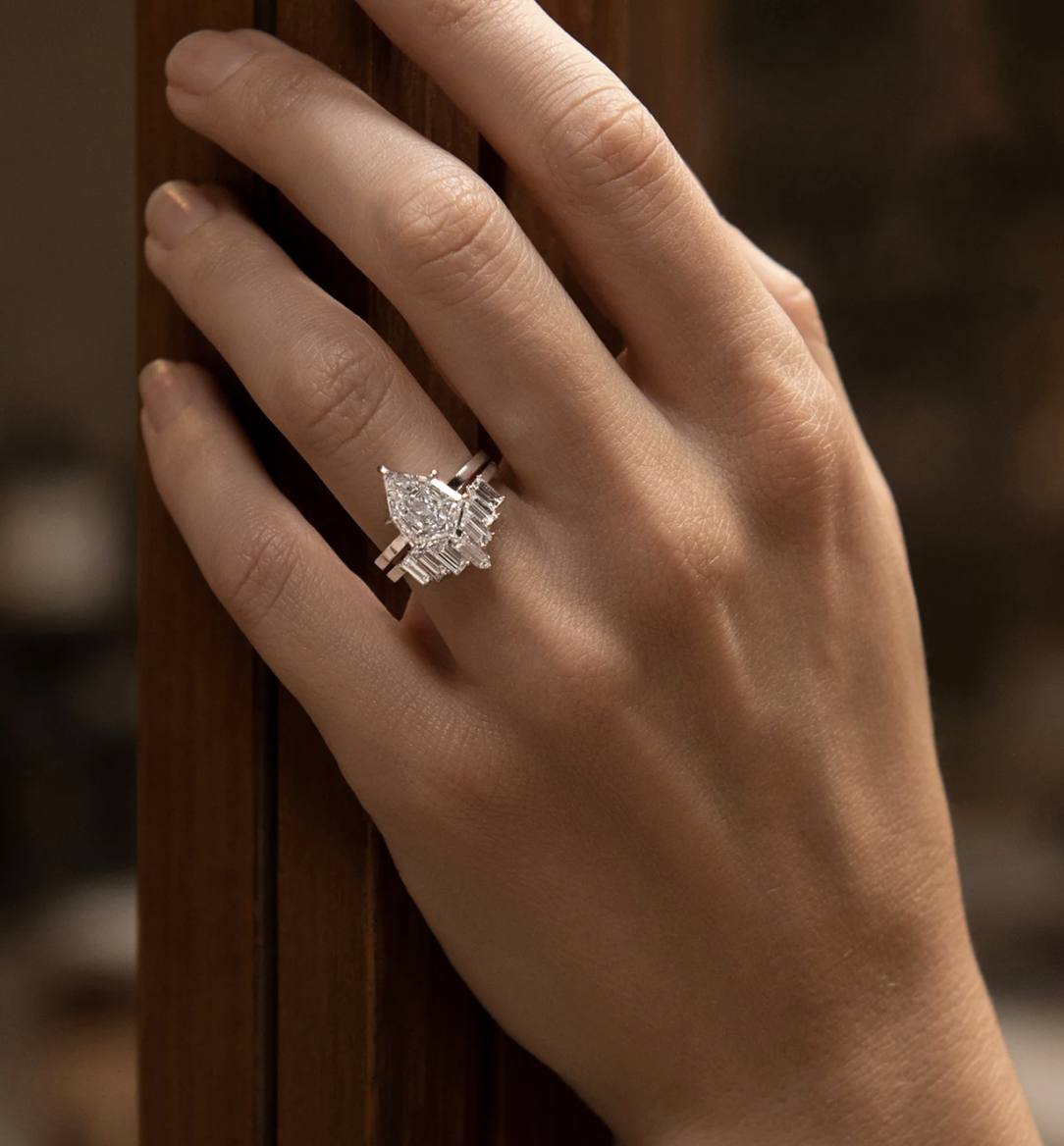 Pear-shaped diamond ring with baguette accents worn on hand beside warm wood