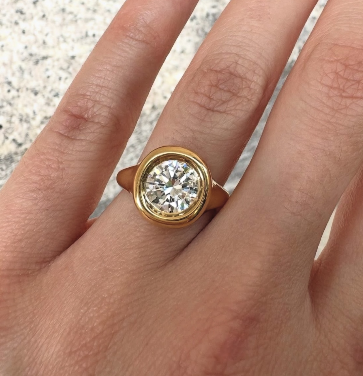 Round bezel-set diamond ring with a tapered gold band worn on hand