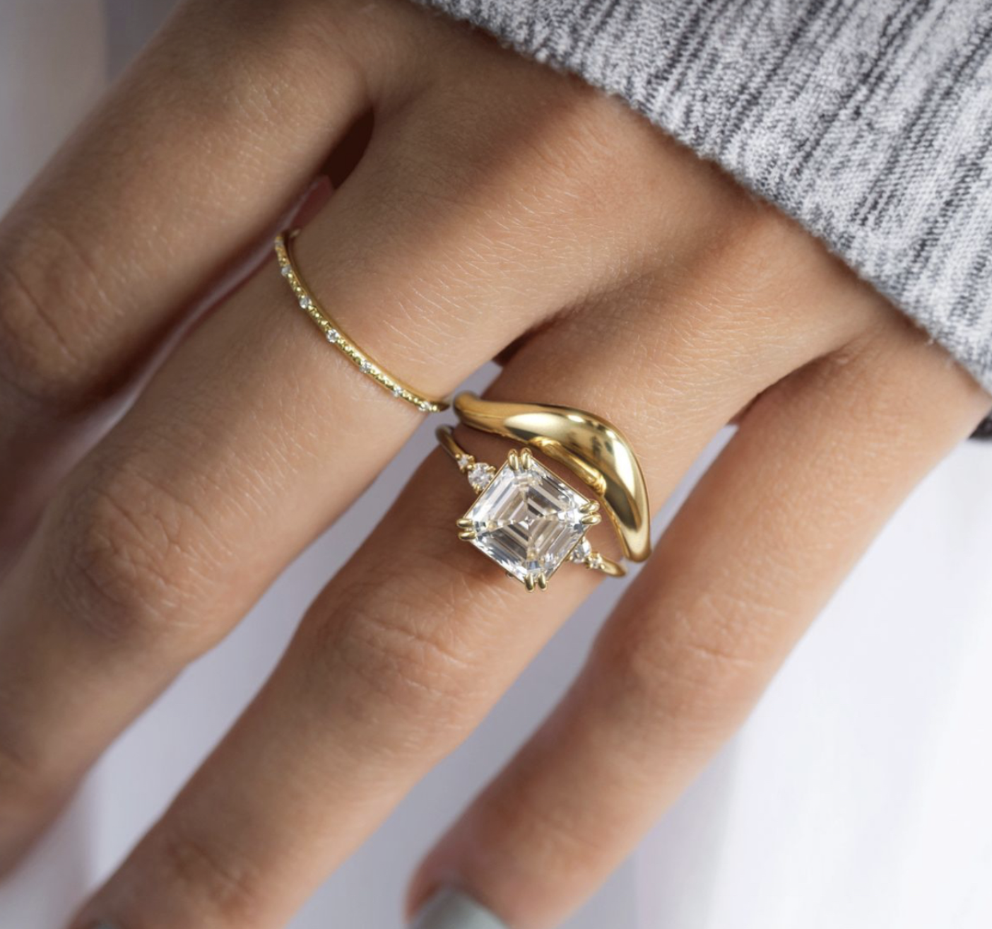 Asscher-cut diamond ring stacked with sculptural gold bands worn on hand